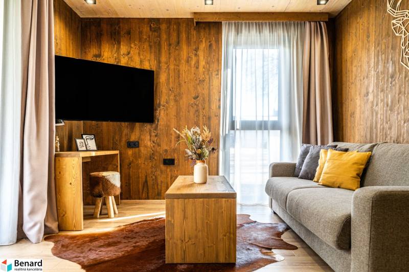 Obývací pokoj v 2-pokojovém bytě s pohovkou, podlahou s dřevěným dekorem a konferenčním stolkem.