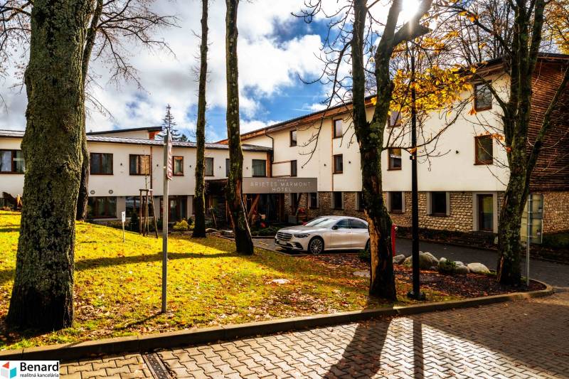 Budova hotelu v Štrbě na Lúčnej obklopená stromy, se zaparkovaným autem.