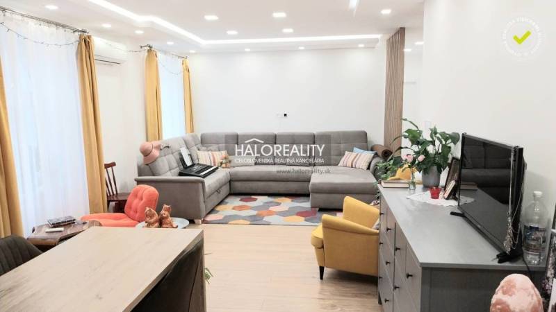 Obývací pokoj v 3-pokojovém bytě s podlahou s dřevěným dekorem, šedou sedačkou a žlutým křeslem.