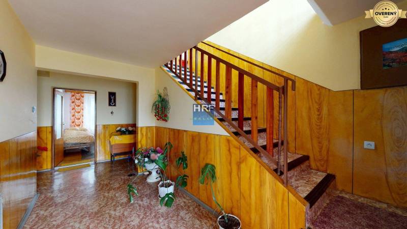 Chodba s dřevěným obložením, schodištěm a pokojovými rostlinami v rodinném domě.