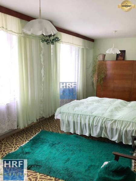 Ložnice v rodinném domě s koberci, záclonami a dřevěnou skříní.