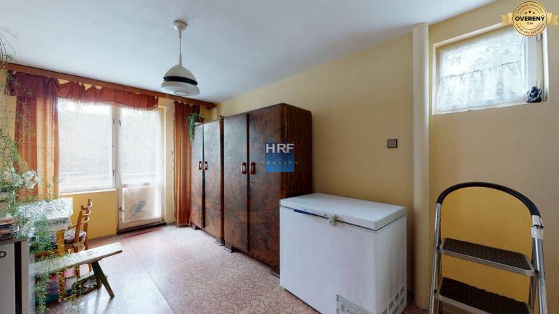 Interiér rodinného domu s mrazničkou, skříňkami a velkým oknem.