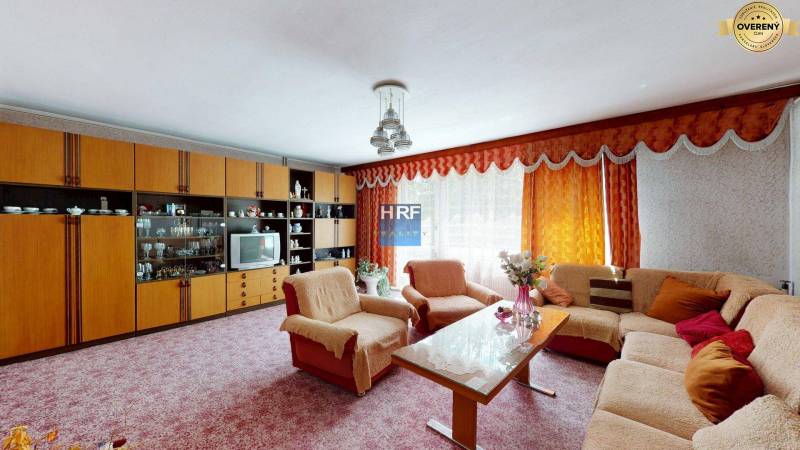 Obývací pokoj v rodinném domě se sedací soupravou, obývací stěnou a květinami.