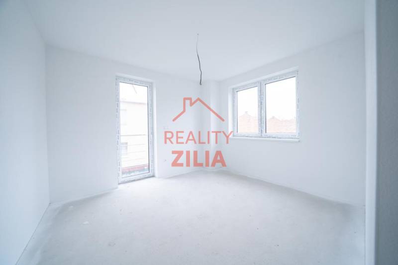 Prázdná místnost v rodinném domě s bílými stěnami a velkými okny.