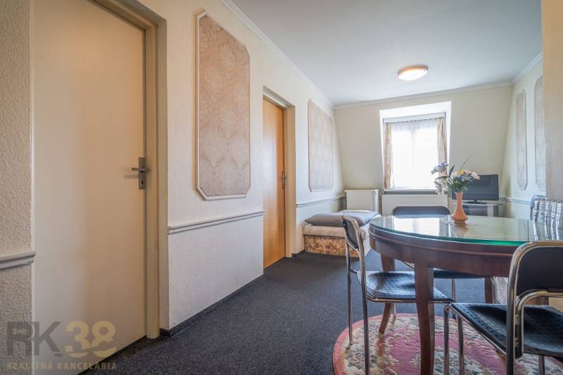 Interiér hotelu a penzionu s kulatým stolem, koberec, TV a ozdobné stěny.