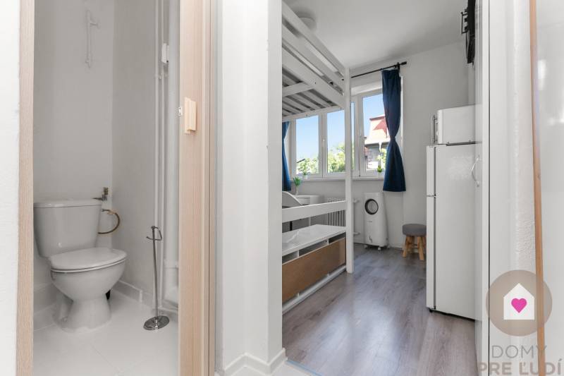 Garsonka s palandou, toaleta a podlaha s dřevěným dekorem ve světlém interiéru.