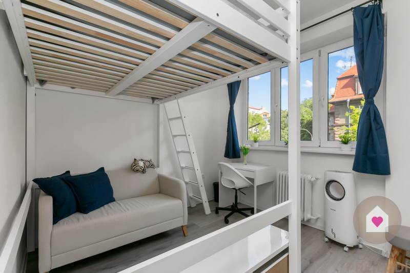 Garsonka s patrovou postelí, pracovním koutem a pohovkou, podlaha s dřevěným dekorem.