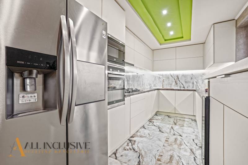 Kuchyně v rodinném domě s bílými skříňkami, mramorovým obkladem a nerezovou lednicí.