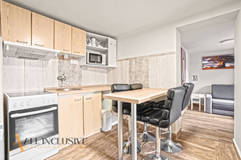 Kuchyně v rodinném domě s barovým stolem, černými židlemi a podlahou s dřevěným dekorem.