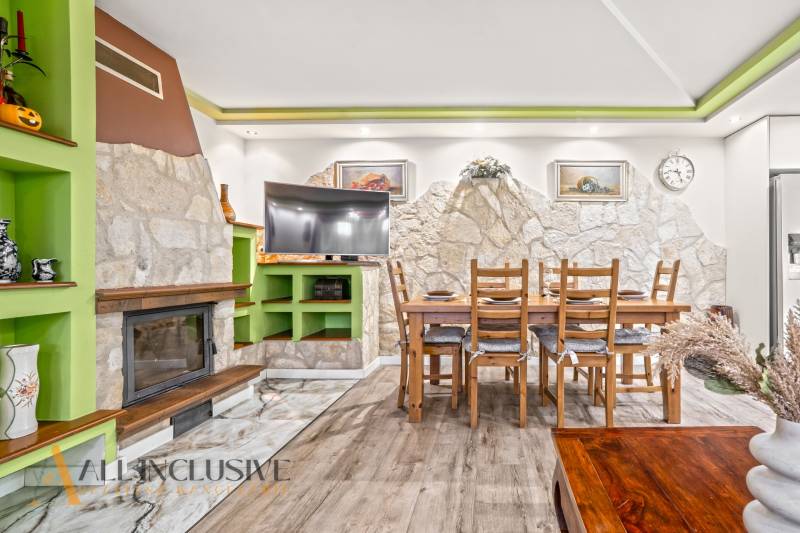 Interiér rodinného domu s krbem, kamennou stěnou, jídelním stolem a podlahou s dřevěným dekorem.