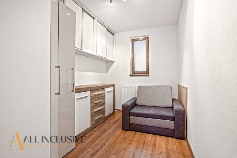 Pokoj v rodinném domě s podlahou s dřevěným dekorem, šedou sedačkou a úložnými skříňkami.