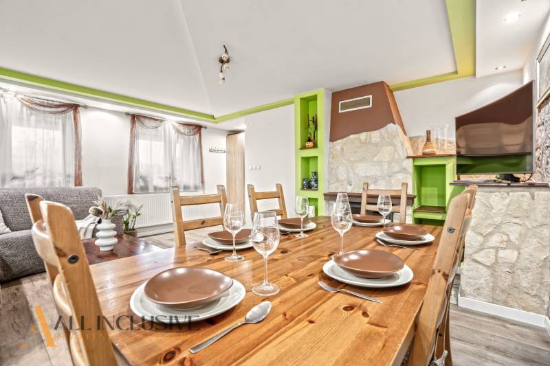 Jídelna v rodinném domě s dřevěným stolem, sklenicemi a dekorativním krbem.