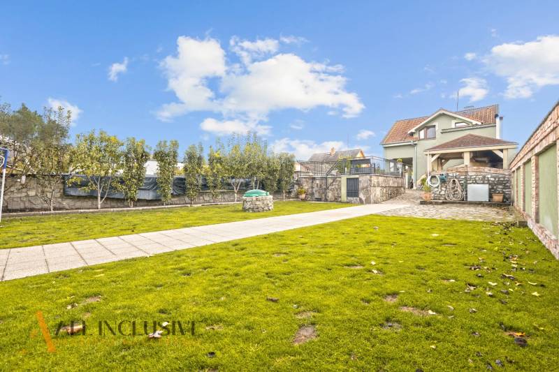 Zahrada rodinného domu na Kúpeľnej ulici v Dunajské Stredě s udržovaným trávníkem a stromy.