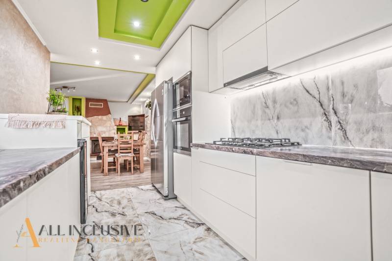 Kuchyně rodinného domu s bílými skříňkami, kamennou deskou a dekorativním stropem.