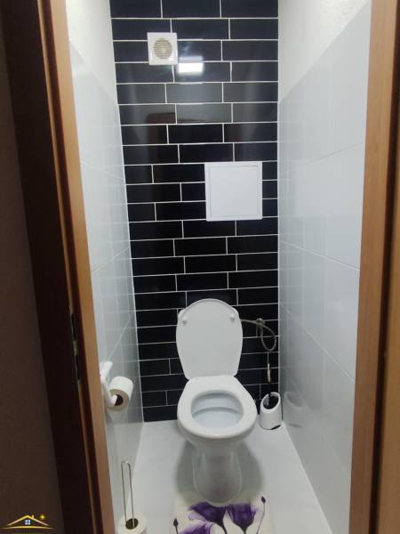 Toaleta s černým obkladem ve 3pokojovém bytě, doplněná bílým sanitárním vybavením.
