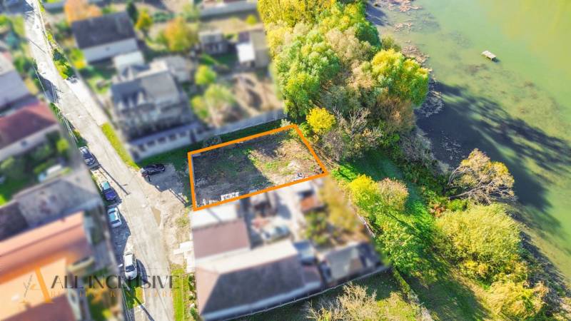 Pozemky - bydlení v Jahodné u řeky, lemované stromy a bohatou zelení.