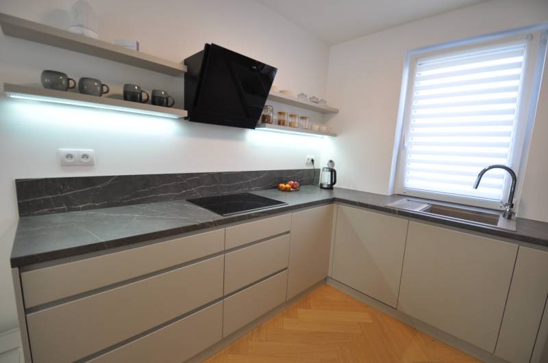 Kuchyně v rodinném domě s tmavou pracovní deskou a podlahou s dřevěným dekorem.