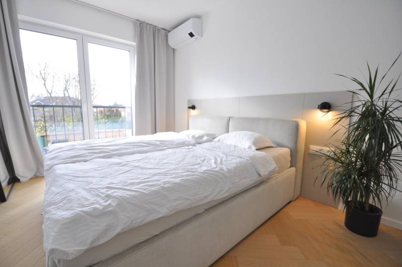 Ložnice v rodinném domě s postelí, rostlinou a podlahou s dřevěným dekorem.