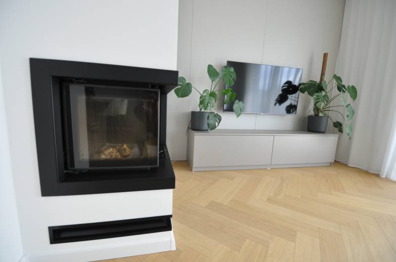 Obývací pokoj v rodinném domě s krbem, televizí a podlahou s dřevěným dekorem.