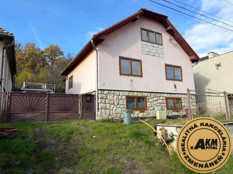 Rodinný dům ve Staré Kremničce se svažitou zahradou a kamennou fasádou.