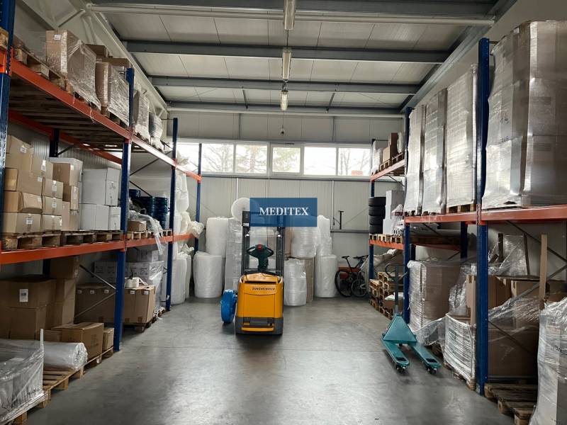 Sklady a haly plné palet a balíků, viditelný vysokozdvižný vozík.