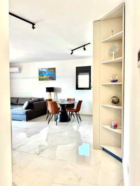 Interiér 1-pokojového bytu s bílou podlahou, šedou pohovkou a jídelním stolem.