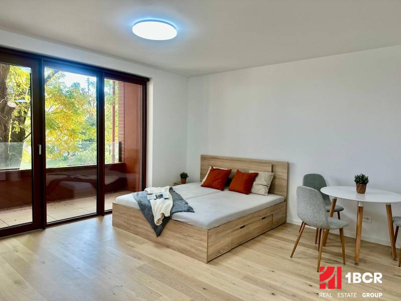 1-pokojový byt s postelí, stolem a podlahou s dřevěným dekorem.