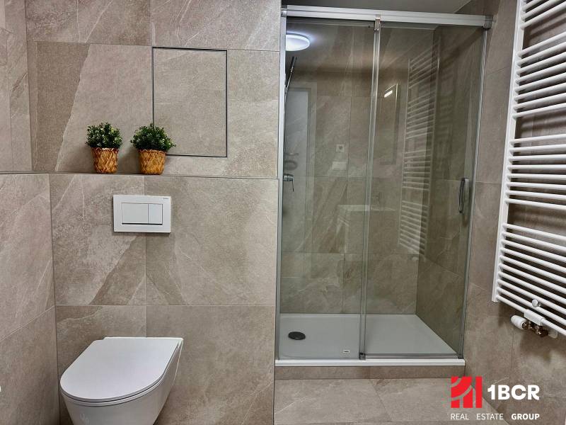 Koupelna v 1-pokojovém bytě s toaletou, sprchovým koutem a živými rostlinami v košících.