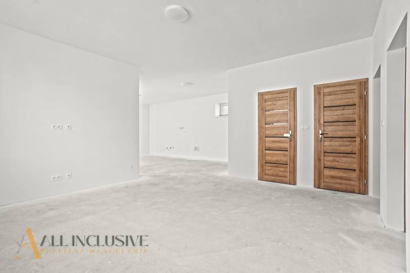 Bílé stěny a dřevěné dveře v interiéru rodinného domu s podlahou bez dekoru.