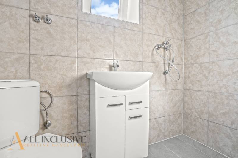 Koupelna v rodinném domě s umyvadlem, sprchou a toaletou ve světlých obkladech.