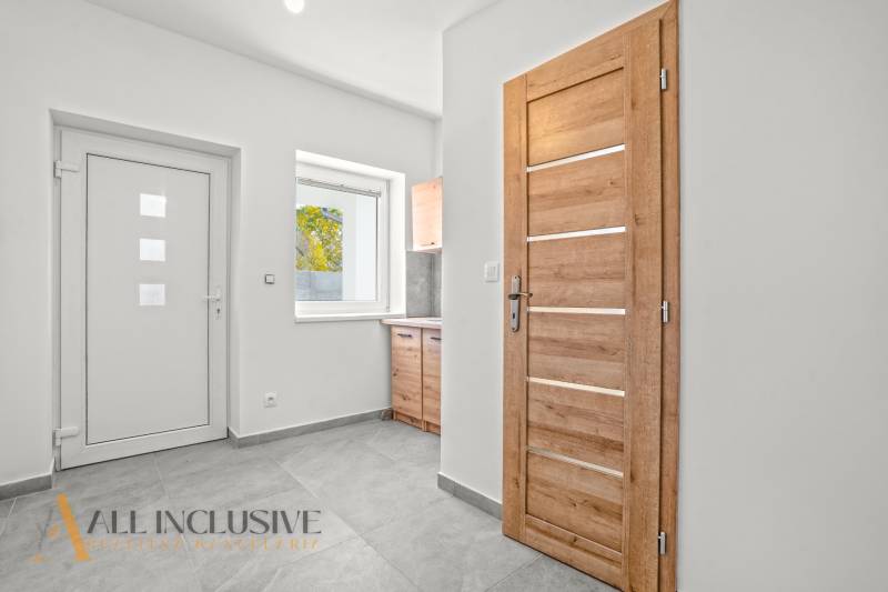 Bílá chodba Rodinného domu s dřevěnými dveřmi a keramickou podlahou.