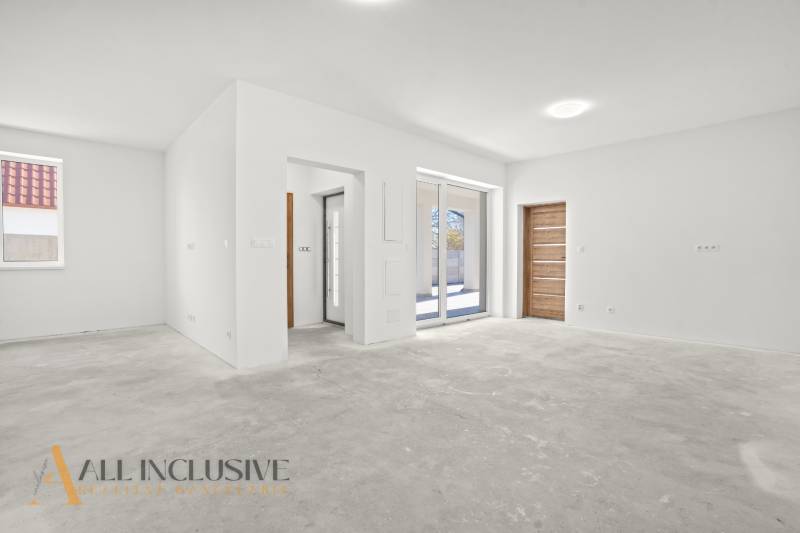 Prostorný interiér rodinného domu s bílými stěnami a dlažbovou podlahou.