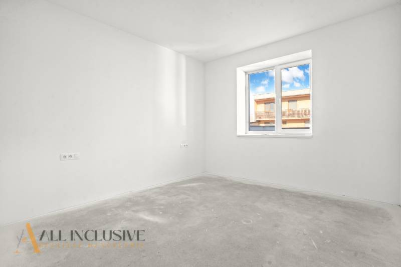 Prázdná místnost s oknem, bílé stěny, výhled na budovu z rodinného domu.