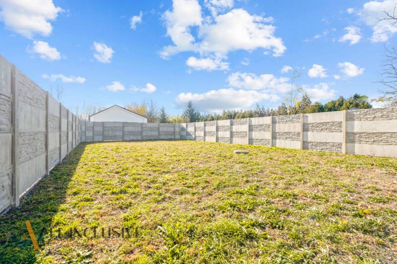 Zahrada rodinného domu v Orechové Potôni s betonovým plotem a travnatým povrchem.