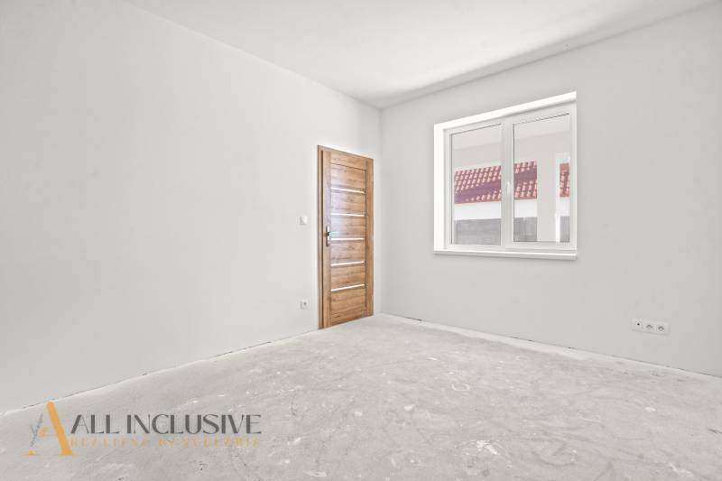 Rodinný dům s bílou stěnou a dřevěnými dveřmi, okno s výhledem na střechu.