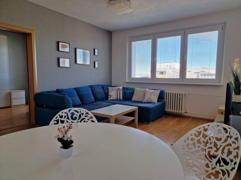 Obývací pokoj 3-pokojového bytu s pohovkou, bílým stolem a podlahou s dřevěným dekorem.