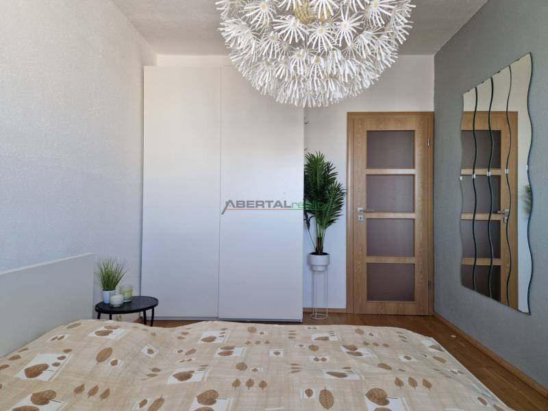 Ložnice s dekorativním svítidlem, šatní skříní a podlahou s dřevěným dekorem v 3-pokojovém bytě.