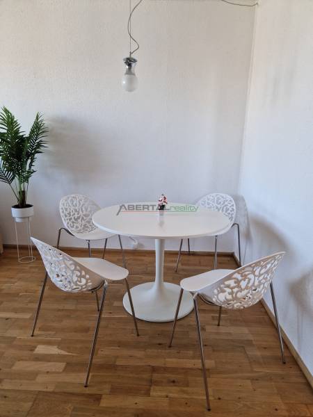 Jídelní kout ve 3-pokojovém bytě s podlahou s dřevěným dekorem a ozdobnými židlemi.