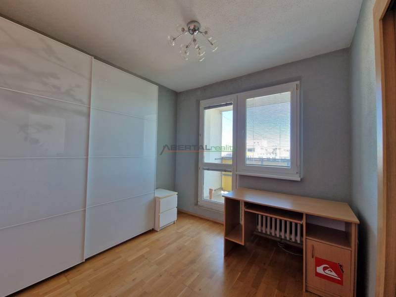 Pokoj v 3-pokojovém bytě s podlahou s dřevěným dekorem, stolem a skříní.