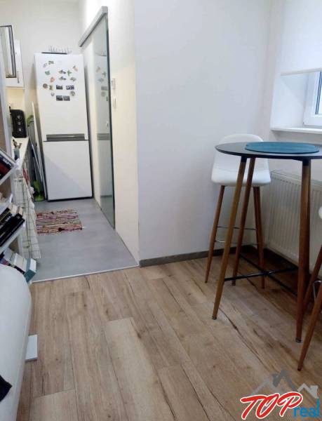 Kuchyně v 1-pokojovém bytě s podlahou s dřevěným dekorem, vysoký stůl a židle.