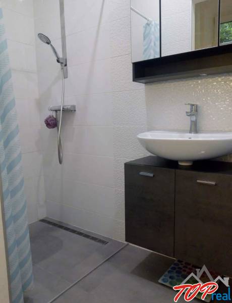 Koupelna s moderním sprchovým koutem v 1-pokojovém bytě, světlé obklady, umyvadlo.