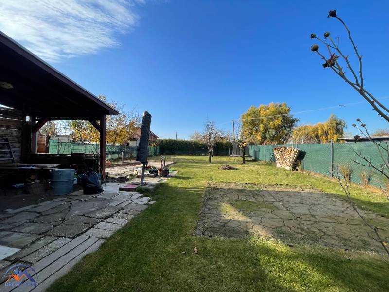 Zahrada u chaty na ulici Nová osada v Komárně, s trávníkem a altánkem.