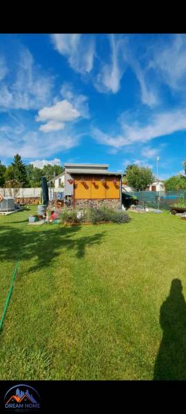 Zahrada u chaty v Nové osadě v Komárně s modrou oblohou a upraveným trávníkem.