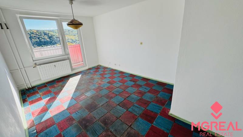 Pokoj v 1-pokojovém bytě s barevnou podlahou a velkými okny, výhledem na přírodu.