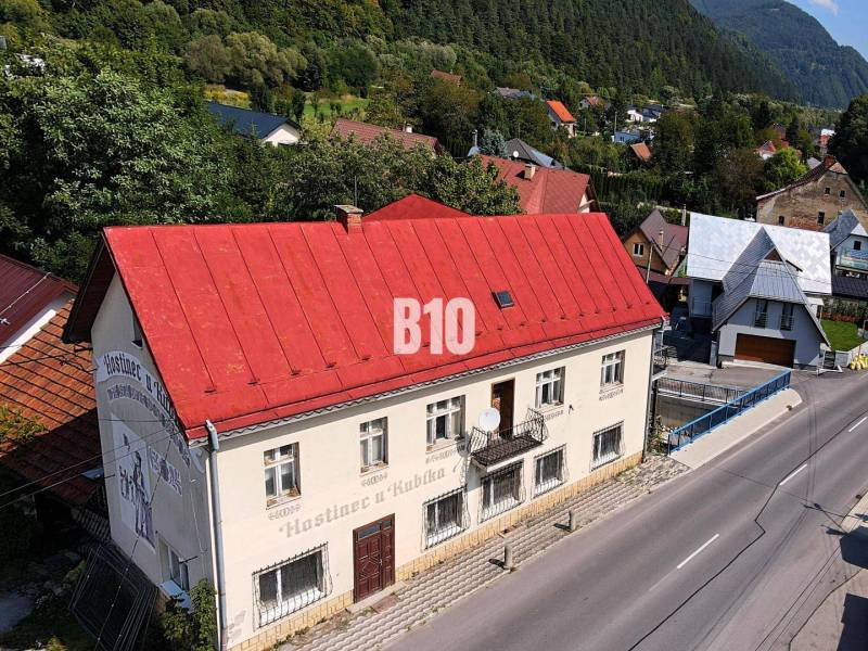 Budova v Belej s červenou střechou na hlavní ulici obklopená zelení a domy.