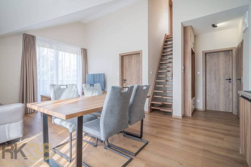 Obývací pokoj s jídelním stolem a schodištěm v 2pokojovém bytě, podlaha s dřevěným dekorem.