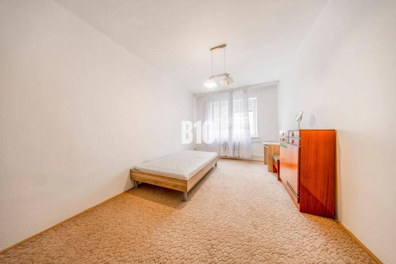 Ložnice ve 4pokojovém bytě s postelí, komodou a kobercem.