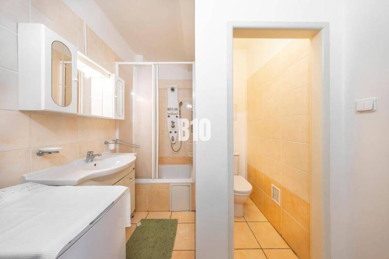 Koupelna ve 4-pokojovém bytě s vanou, skříňkami a toaletou, laděná ve světlých barvách.