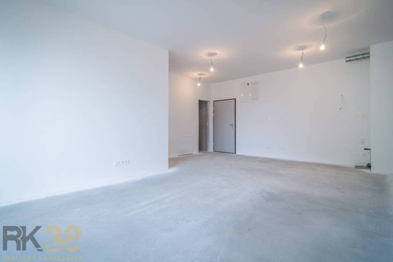 Prostorný obývací prostor v 2pokojovém bytě, bílé stěny, základní osvětlení.