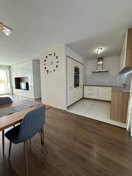 Jídelní prostor ve 4-pokojovém bytě s podlahou s dřevěným dekorem a kuchyní v pozadí.